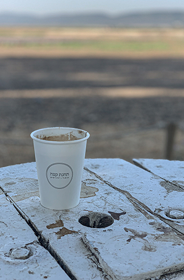 כוס קפה על גלגל עץ מול השדות בעגלת הקפה תחנת קפה