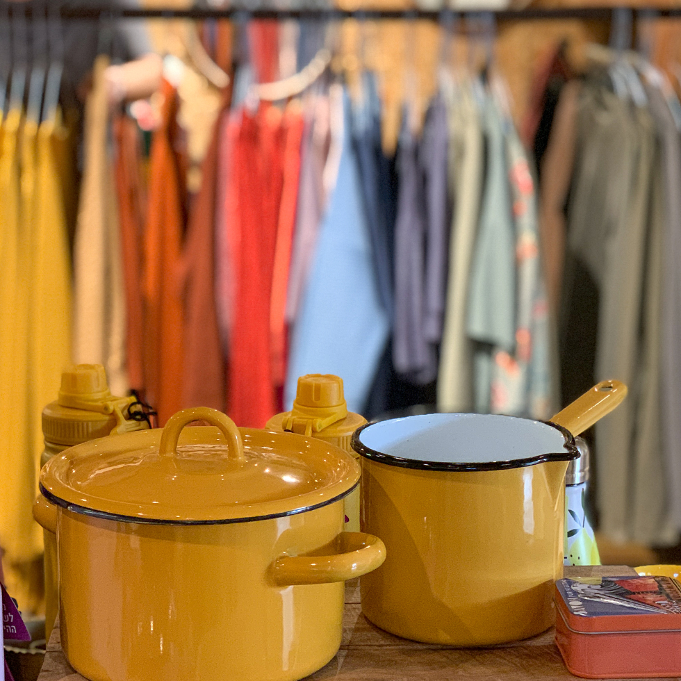 סירי אמייל צהובים ובגדים תלויים על קולב בחנות רבקה Rebecca בקיבוץ נען