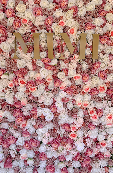 קיר פרחים ורדים מלאכותיות בוורוד ולבן וכיתוב באותיות זהב גדולות באנגלית - MIMI בכניסה לגלידריה מימי בזכרון יעקב
