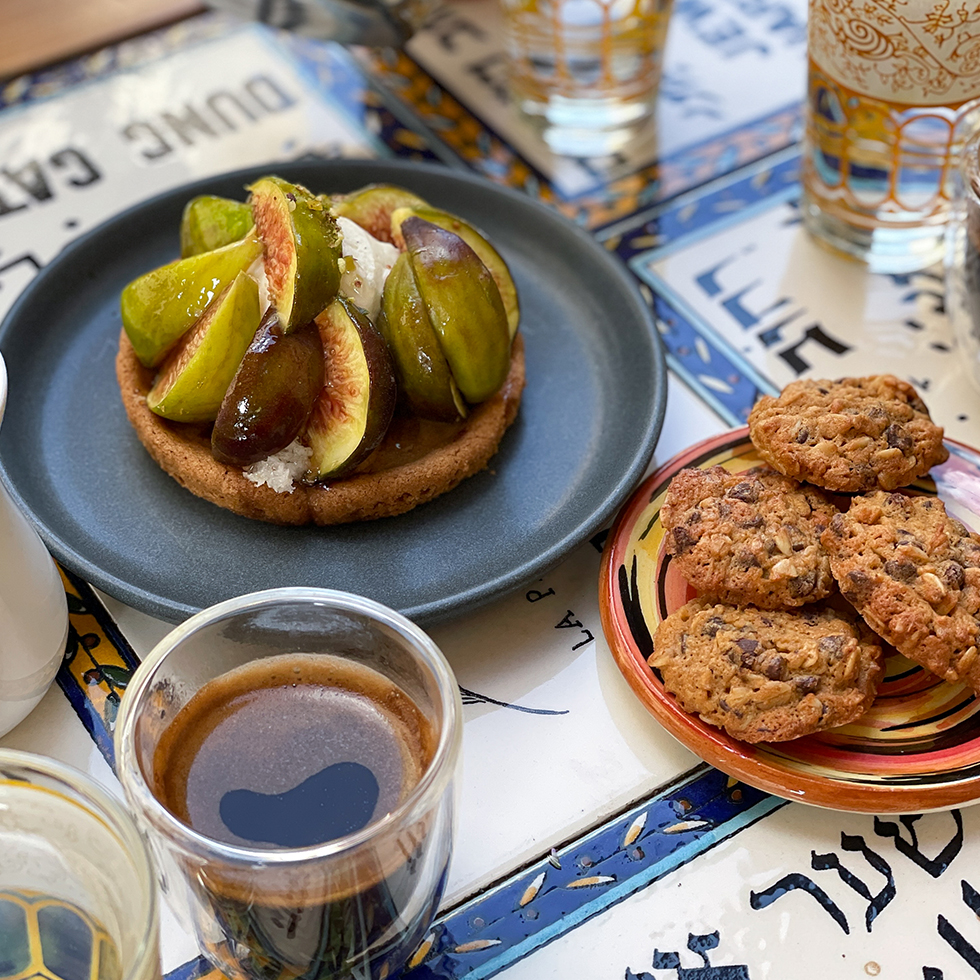 כוס אספרסו, עוגיות שוקולד צ'יפס ועוגת תאנים על שולחן עם אריחים מצוירים בעיר העתיקה בירושלים
