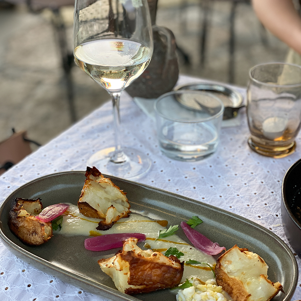 מנה של תפוחי אדמה צלויים וברקע כוס יין לבן במסעדת פיגם בעין הוד