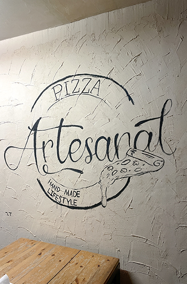 ציור קיר עם המילים פיצה ארטיזנל באנגלית בפיצה טריילר בכפר האומנים ביישוב צוקים