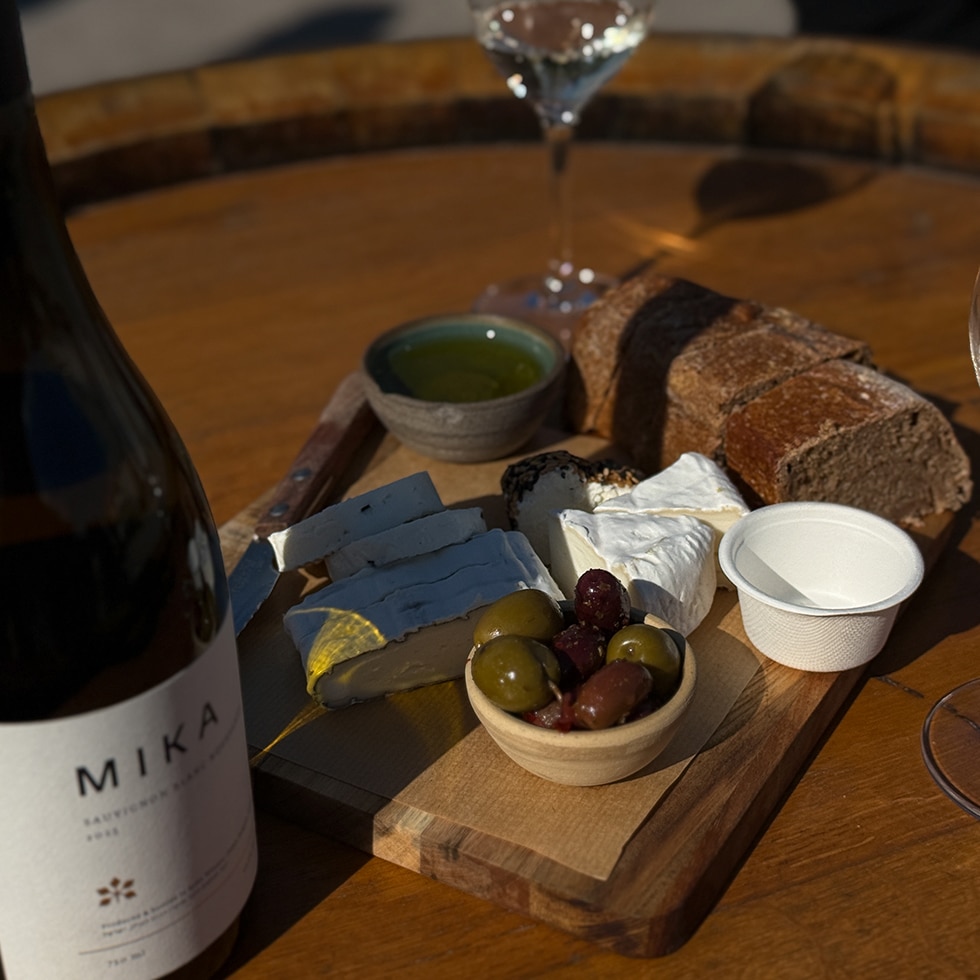 פלטת גבינות, זיתים, שמן זית ולחמים, לצד כוס יין ובקבוק יין ביקב מיקה במושב בני יהודה